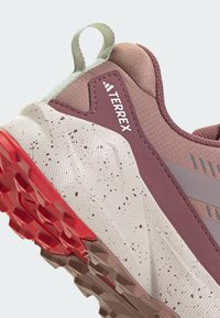 Terrex Trail-Schuh mit pinkem Obermaterial, beiger Zwischensohle mit Sprenkeln und roter Laufsohle mit strukturierten Griffigmustern.