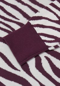 Gros plan sur un pull rayé zèbre violet et blanc, montrant un poignet violet côtelé et un tissu tricoté texturé.