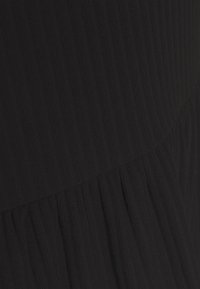 Tissu noir à côtes avec des rayures verticales, présentant une texture froncée en bas. Le matériau semble doux et légèrement extensible.