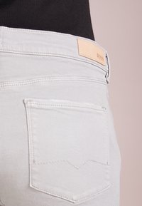 Grå denimjeans med en enkel bakficka med ett subtilt sömnadsmönster och en beige läderlogotyp. Mjuk textur, slim fit-design.
