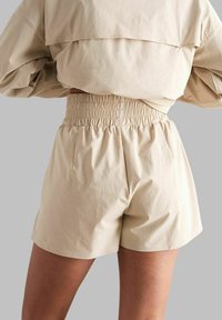 Shorts beiges avec une ceinture smockée, des poches latérales et une texture lisse, associés à un haut assorti.