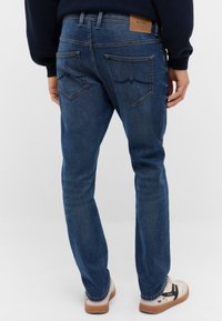 Šviesiai mėlyni džinsai su tiesiu sijonu, dekoratyvine siuvinėjimu ant galinių kišenių ir odiniu etiketėmis ant juosmens.