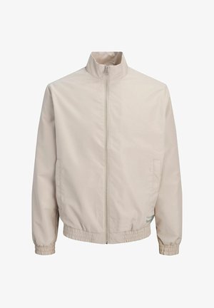 Veste beige zippée avec col montant, poignets élastiques, ceinture élastique et poches latérales, présentée sur fond blanc.