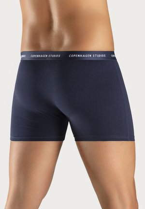 Navy blue cotton boxer shorts with a white "Copenhagen Studios" branded waistband. Smooth texture and fitted design with no patterns.
