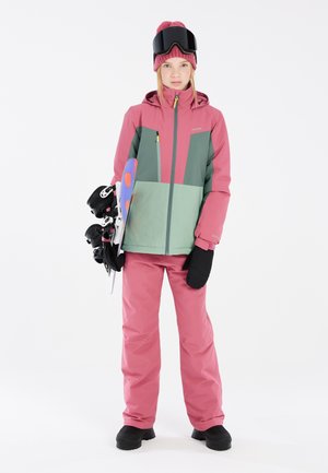 Zweifarbige Winterjacke in Pink und Grün mit Reißverschlusstaschen, kombiniert mit passenden pinken Hosen, schwarzen Handschuhen und einem bunten Snowboard.