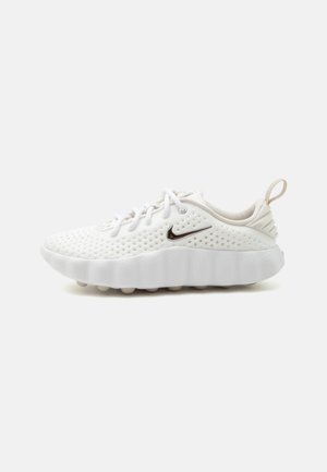 Hvid Nike-sneaker med perforeret overdel, metallisk swoosh-logo, tyk polstret sål, snørebånd og trækflig på hælen.