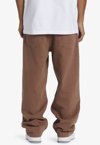 Bruna säckiga byxor i ett strukturerat tyg, med hög midja, bakfickor och uppvikta fållar, kombinerade med vita sneakers.