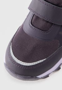 Zapatilla deportiva morada con parte superior de malla, acentos sintéticos, correa de gancho y bucle, puntera redondeada y suela de goma con detalles en color claro.