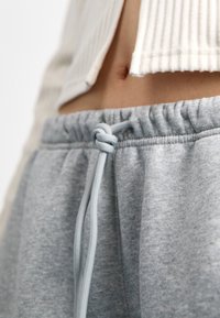 Graue Jogginghose mit Kordelzug bestehen aus einem weichen Stoff mit glatter Textur und präsentieren ein geknotetes Kordeldetail am Bund.