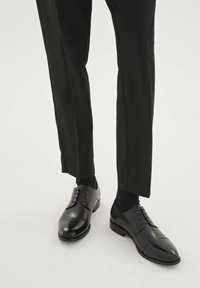 Chaussures habillées en cuir noir avec une finition lisse, bout arrondi et design à lacets ; associées à des chaussettes foncées et un pantalon noir ajusté.