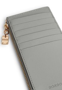 Grijze leren portemonnee met gouden rits, zes kaartsleuven, subtiele verticale lijnen en een gouden hardware logo label. Glad textuur.