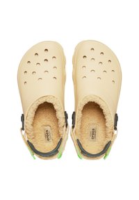 Beige klipklappere med blødt, fuzzy for, flere ventilationshuller, justerbare hælstrapper og en struktureret gummisål.