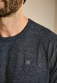Polo majica tamnoplave boje izrađena od teksturirane tkanine s suptilnim prugastim uzorkom i malim izvezenim logom na lijevoj strani prsnog koša.