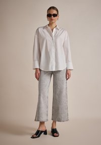 Camicia bianca con bottoni, pantaloni ampi in denim grigio chiaro, mule nere con tacco, e occhiali da sole neri a forma quadrata. Tessuto liscio e orli sfrangiati.
