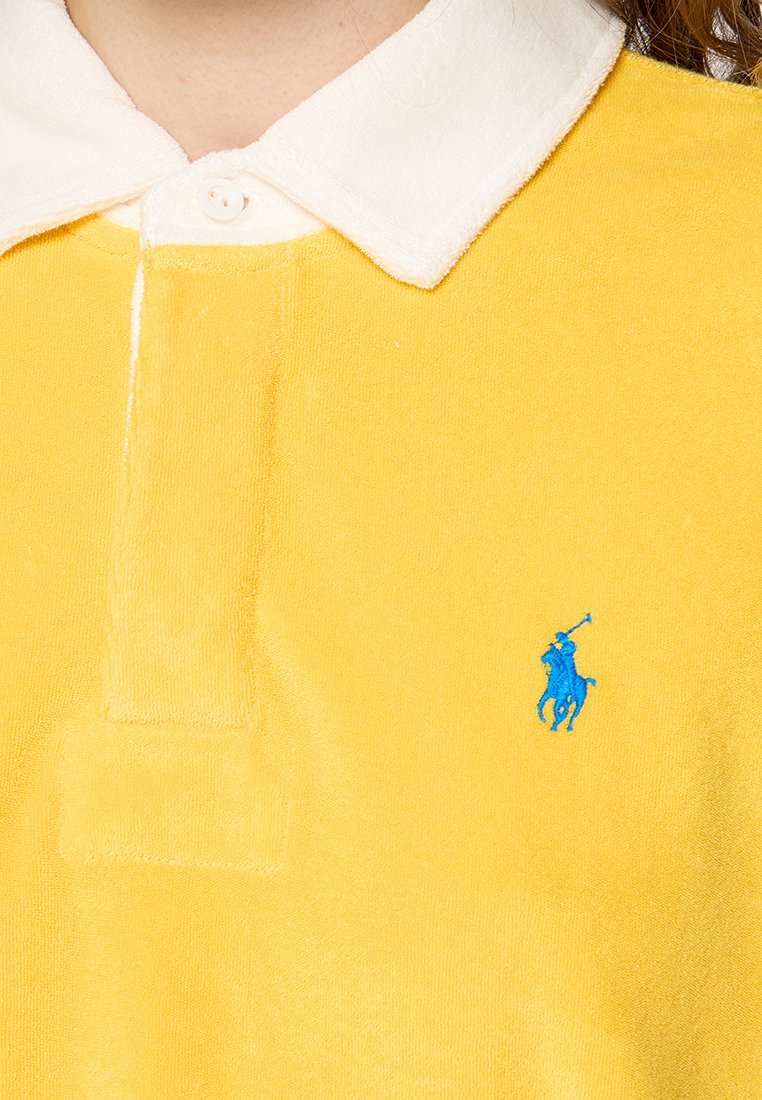 Polo shirt giallo in maglia con colletto bianco, patta con tre bottoni e logo ricamato blu di un cavaliere sul lato sinistro del petto.