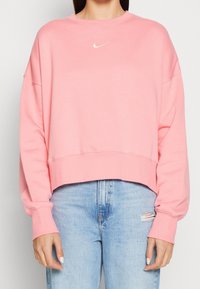 Sudadera rosa corta, tela suave, puños anchos, dobladillo y cuello acanalados; con pequeño logo blanco de Nike en el pecho.