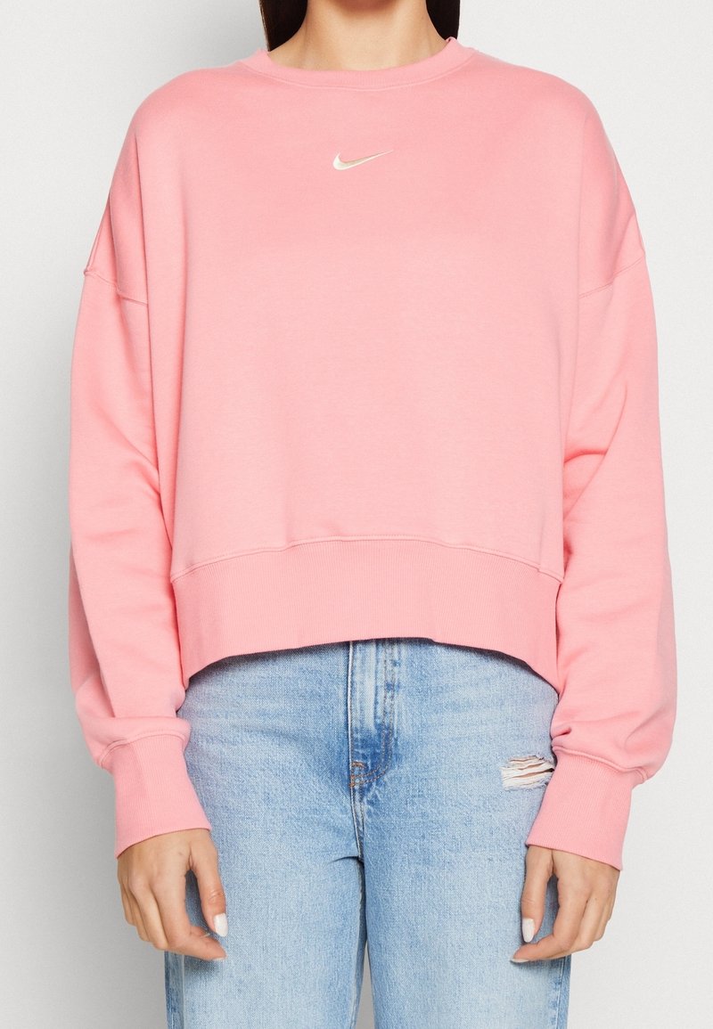 Sudadera rosa corta, tela suave, puños anchos, dobladillo y cuello acanalados; con pequeño logo blanco de Nike en el pecho.