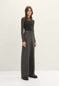 Haut noir à manches longues avec une texture transparente, associé à un pantalon large gris foncé. L'ensemble présente une finition lisse et une coupe décontractée.