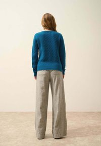 Tealstickad tröja med texturerat mönster och ribbad fåll, kombinerad med högmidjade grå vida byxor i randig tyg.