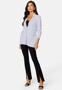 Blazer lilla chiaro con un solo bottone, due tasche frontali e maniche a tre quarti, abbinato a pantaloni neri con spacchi laterali.