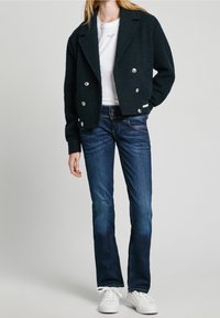 Svart dubbelknäppt jacka med silverknappar över en vit t-shirt, i kombination med mörkblå utsvängda jeans och vita sneakers.