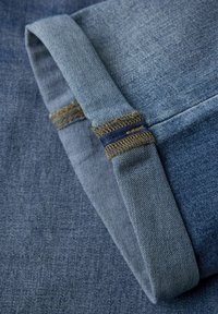 Denim tkanina u raznim tonovima plave boje, s povijenim manžetama i kontrastnim šavovima te teksturiranim završetkom.