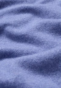 Blauwe brei-stof met een zachte textuur, die een glad oppervlak en subtiele variaties in tint toont. Geen duidelijke patronen of hardware zichtbaar.