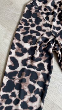 Stoff med svart og brunt uregelmessig leopardmønster på lys beige bakgrunn, lagt flatt på en lys tremateriale.