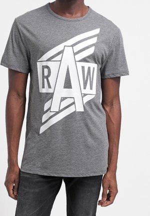  camiseta gris de manga corta con un gran estampado gráfico blanco que presenta las letras "RAW" y acentos estilizados. Corte regular con escote redondo.