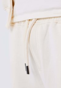 Pantalones joggers de color beige claro con cintura ajustable, que presentan una textura suave y detalles en hardware plateado en los extremos del cordón.
