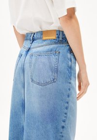Lichtblauwe denim jeans met een hoge taille, voorzien van een bruine leren label aan de achterkant en twee achterzakken. De stof heeft een licht vervaagde textuur.