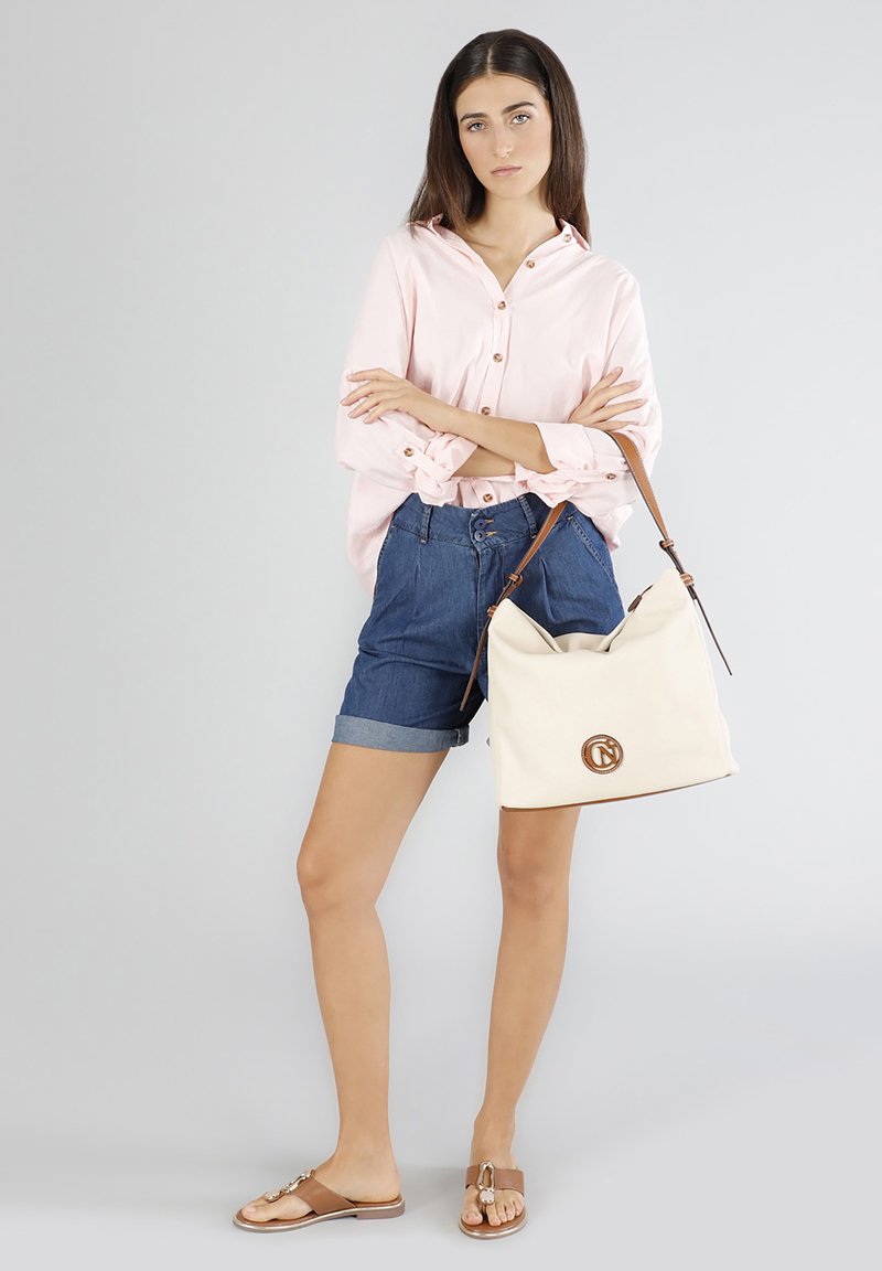 Lichtroze overhemd met knopen, denim shorts, bruine sandalen en een beige canvas handtas met logo-detail en leren accenten.