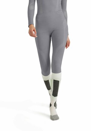 Graue Sportleggings mit einem figurbetonten Design, ausgestattet mit strukturierten Akzenten und einem hohen Bund, kombiniert mit weißen und grauen Socken mit dunklen Flecken.