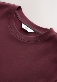 Burgundy sweatshirt with a crew neck and ribbed collar; soft, smooth texture; branded label displaying "NEXT REGULAR FIT" inside.