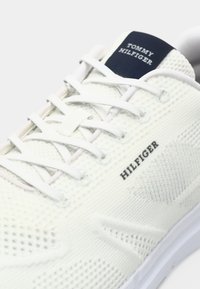 White knitted sneaker with white laces, "Hilfiger" on the side, and a navy label on the tongue reading "Tommy Hilfiger."