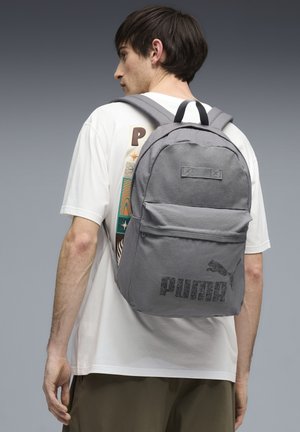 Grå stofrygsæk med justerbare stropper, forlomme og trykt "PUMA"-logo. Har et topgreb til bæring.