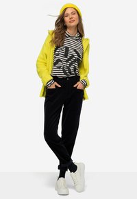 Gele fluffy cardigan, zwarte corduroy broek, gestreepte zwart-witte turtleneck met grafisch ontwerp, witte sneakers, gestyled met een bijpassende beanie.