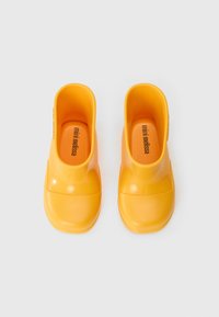 Sabots en caoutchouc jaunes avec des orteils arrondis et un design à enfiler. L'intérieur présente la marque "mini melissa" ; texture lisse et finition brillante.