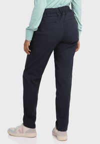 Marineblaue, elastische Hose mit lockerer Passform, Gesäßtaschen und glatter Textur, kombiniert mit hellen Sneakers.