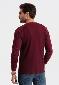 Pitkähihaista viininpunaista ribbid-paitaa, jossa on pyöreä kaula-aukko ja kontrastiväriset raglanhiat, yhdistettynä sinisiin farkkuihin.