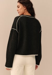 Maglione nero corto con dettagli di cucitura bianca, polsini e bordo a costine, caratterizzato da una vestibilità morbida e una texture delicata.