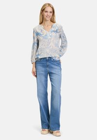 Blusa con stampa floreale in blu e crema, con scollo a V e bottoni. Abbinata a jeans flare in denim chiaro a vita alta e sandali con tacco.