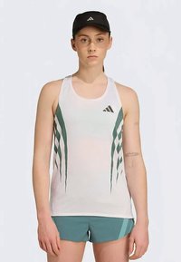 Valge sportlik tank top roheliste diagonaalsete triipudega, kombineeritud teal värvi lühikeste pükstega. Mudel kannab musta mütsi, millel on valge LOGO.