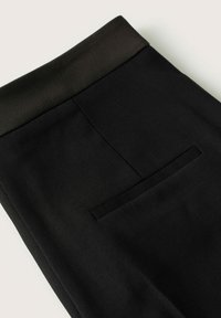 Pantalon noir sur mesure avec une taille lisse, une poche arrière unique et une texture raffinée, mettant en valeur un design classique.