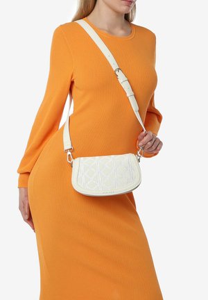 Borsa a tracolla bianca con motivo a rombi trapuntati, caratterizzata da una forma rotonda e una tracolla regolabile, indossata su un vestito arancione a costine.
