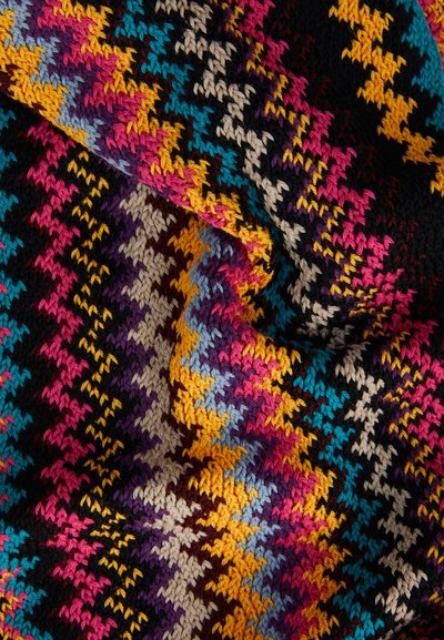 Multikleurige gebreide stof heeft een zigzagpatroon in roze, blauw, geel en zwart, met variërende texturen en aardetinten.