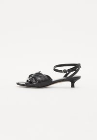 Sandales noires en cuir avec un design noué sur l'orteil, une fine bride de cheville et un petit talon kitten. Texture lisse tout au long.