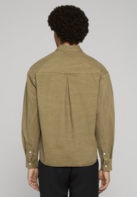 Langärmeliges khakifarbenes Hemd mit lockerem Schnitt, geknöpften Manschetten und einer Falte am Rücken. Verfügt über eine dezente Textur und ein markenbesticktes Etikett am Kragen.