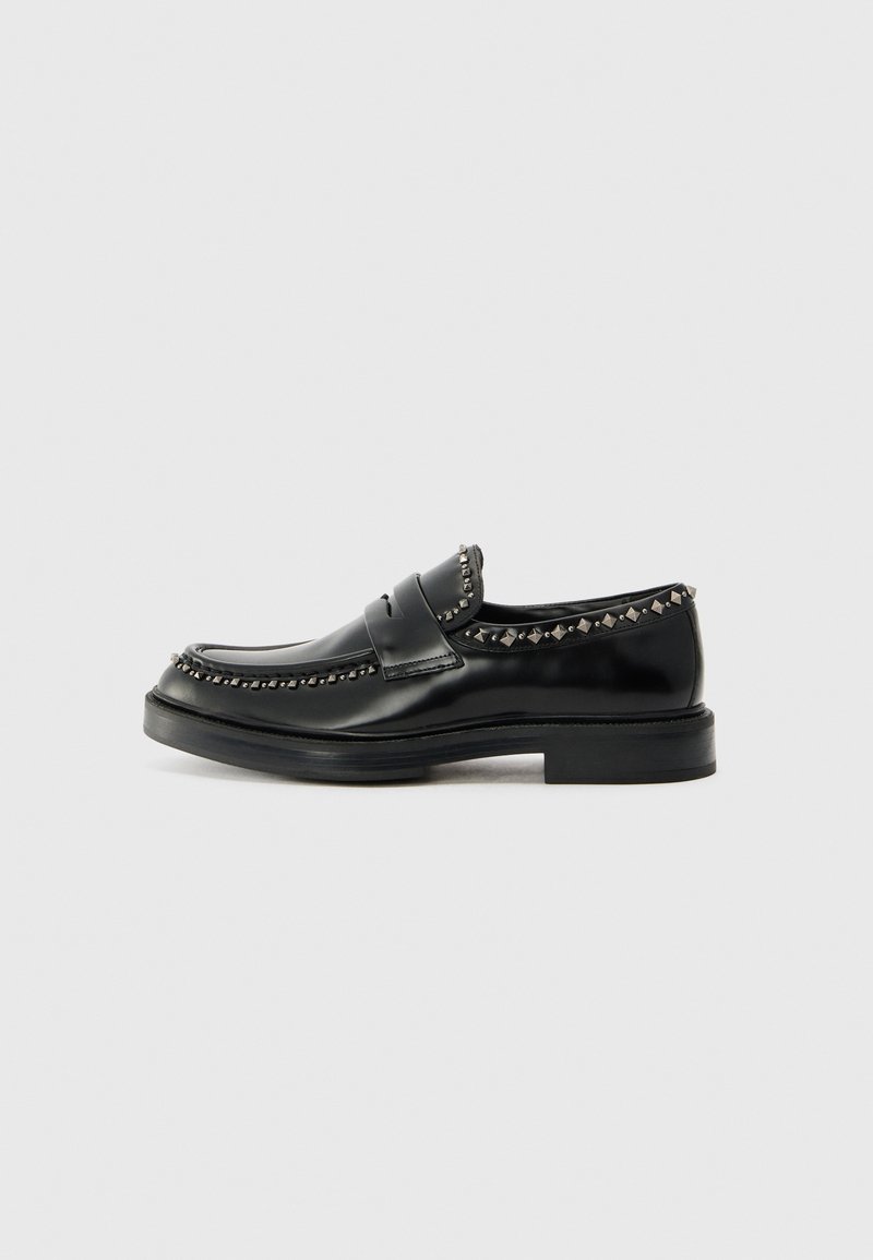Mocassin en cuir noir avec des clous argentés contrastants le long du bord supérieur, doté d'un bout arrondi et d'une semelle en caoutchouc plate.