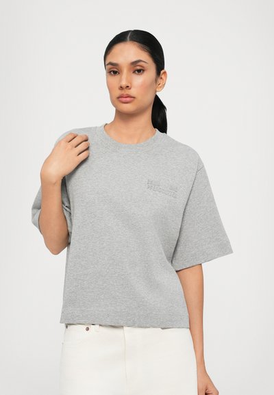 Camiseta de algodón gris con cuello redondo y mangas cortas. Presenta un pequeño logotipo en relieve en el pecho. Corte recto con una textura suave.